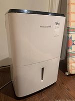 Front view of dehumidifier showing Frigidaire logo, water reservoir level indicator and white housing