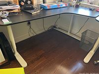 Full view of IKEA black L-shaped corner desk showing white metal legs and black desk surface, no items included.