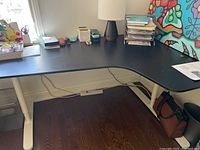 Full view of the black L-shaped desk surface showing the corner design and some office materials on top (not included).