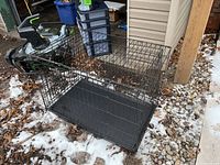 Full view of collapsible metal dog crate with plastic liner taken outside on ground with snow and debris