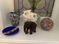 All five items displayed together: wooden elephant, white stone elephant figurine, glass ornament sphere, blue art glass plate, and art glass cup.