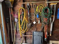 Photo of garden tools and accessories hung on wooden wall including rakes, shovels, hoses, electrical cords, crutches and boot trays