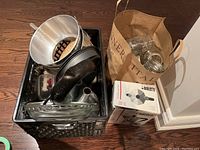 Crate containing various metal bakeware including springform pans, glass pie plates, a Bialetti moka pot box, and a paper bag filled with mason jars.