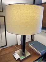 Front view of desk lamp showing cream fabric drum lampshade and a portion of metal base on wooden surface.