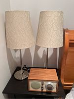 Overview photo showing two table lamps with metal bases and embroidered shades, and the Tivoli Audio Model One radio with wooden casing on a black surface.
