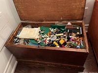 Wooden chest open showing a large pile of assorted LEGO pieces including baseplates and minifigures