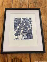 Framed print showing Amsterdam canal scene with buildings and cyclists, set on wooden floor.