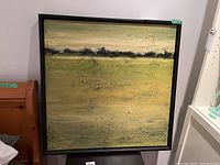 Framed square abstract landscape painting showing horizontal bands of color in muted greens and tans with a dark band and textured thick paint.