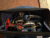 Open work bag showing multiple Ryobi cordless tools including circular saw, reciprocating saw, and work light in the bag