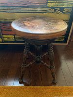 Front view of antique hardwood stool showing round worn seat and four turned wood legs with metal feet