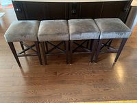 Four matching bar stools arranged in a row showing light grey upholstered seats and dark wood legs.