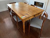 Perspective showing table with chairs around it, visible drawer on side, scuffs and scratches on wooden surface.