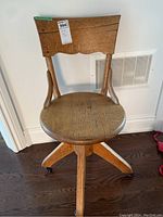 Front view of vintage wooden desk chair showing scalloped top-back design, round seat, and wheel casters on legs.