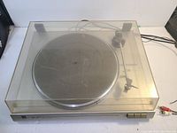Turntable with transparent dust cover showing platter, tonearm, and cartridge with needle. Shows general condition and setup of the device.