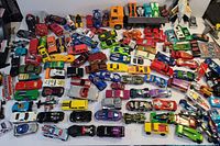 Top view showing approximately 60+ die cast cars in various colors and models spread out on a white surface.