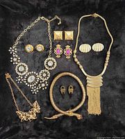 All nine pieces of vintage jewelry displayed on black background. Four necklaces and five pairs of earrings visible showing a variety of styles including floral, snake motif, and geometric shapes with rhinestones and gold tones.