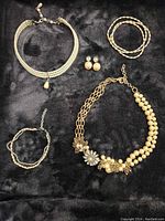 Full lot view including 2 necklaces, 2 bracelets, and 1 pair of earrings arranged on black fabric background.