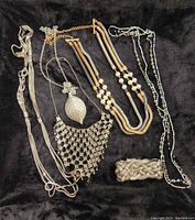 Full overview of five necklaces arranged with a braided silver tone bracelet with magnetic clasp on a black fabric background.