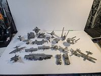 Full view of 22 metal mini models laid out on white surface, showing variety of ships, planes, landmarks, and vehicles