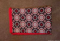 Folded view of bedspread side with white and red concentric circles and red fringe.