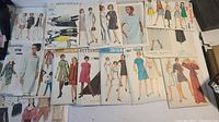 Lot of assorted vintage sewing patterns from various brands laid out flat showing illustrated envelopes with designs of women and children clothing.