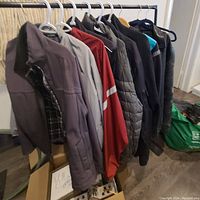 Nine men's jackets in a row on hangers, showing a variety of styles and colors including grey, red, black, and blue tones.