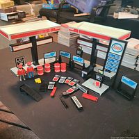 Wide-angle image showing the entire Playmobil Esso gas station set with figures and accessories laid out on a black surface.