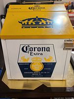 Front view showing yellow lid with blue crown and Corona Extra logo on the white front panel