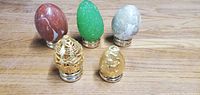 Five heavy collectible eggs displayed on metal stands on a wood surface.