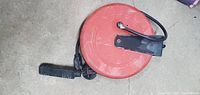 Top down view of a red circular metal electrical cord retractable reel with black electrical cord and plug extending from it.
