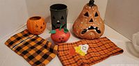 Five pumpkin-themed Halloween decor pieces arranged on two Halloween cloths against white background