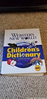 Front cover of Webster's New World Children's Dictionary Second Edition, showing title, edition, and colorful images including apple and dinosaur.