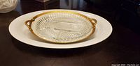 Photo shows large white 14 inch round platter with a smaller gold rimmed decorative plate on top placed on dark surface.
