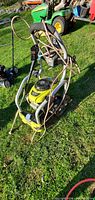 Ryobi power washer standing on grass, showing front view with attached hose and spray wand wrapped on frame.