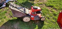 Side view of TroyBilt red self-propelled lawn mower with fabric grass catcher bag on grass surface.
