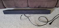 Front view of VIZIO 30" sound bar laid on carpet floor in front of brown couch, showing speaker grille and attached cables.