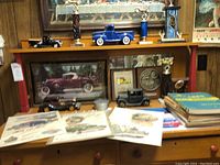 Model vintage cars, trophies, framed wall plaques, and vintage auto parts catalogs including printed advertisements displayed on a wooden dresser.