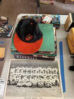 Photo showing Orioles cap, baseball books with one titled 'The Baseball Scrapbook', and Baltimore Orioles 1953 team photo below all items.