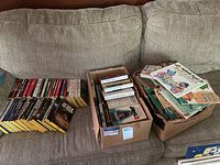 Overview of books laid out on a couch including books arranged flat and in boxes with a mix of colors and sizes visible.