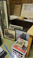 Multiple framed railroad art prints and books on a shelf and floor corner, lace fabric folded on shelf.
