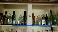Shelf of assorted clear, green, and brown vintage glass bottles showing variety in size and shape