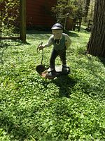 Full view of the jockey statue standing in grass near a tree and building.