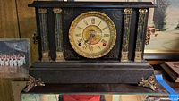 Full frontal view of the vintage black mantel clock with gold decorative columns and base detailing.