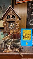 Full frontal view of the cuckoo clock and book showing the carved details, weights, and clock face.