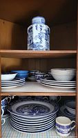 Shelf containing stacks of blue and white plates, bowls, and a round decorative jar on top shelf