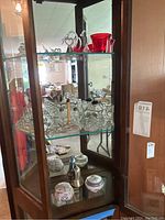 Glass display cabinet with various clear and red glass figurines including swans, glass cars, and decorative items.