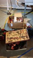 Photo showing a box with assorted vintage and modern Christmas tree ornaments including a boxed set of NOEL figurines.