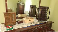 Photo displaying three wooden jewelry boxes on a dresser, including a tall box with drawers, a box with side door, and a flat box, all sitting on a lace runner.