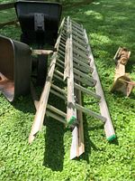 Two aluminum extension ladders with visible dirt and wear laid on grass with some metal parts and other items nearby.