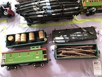 Photo showing green caboose and freight cars, flatbed with metal track pieces in background, wooden barrels and logs as faux contents